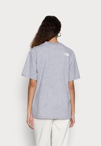 Grå bomullströja med korta ärmar. Har en liten vit logotyp på övre ryggen. Slät textur och avslappnad passform.