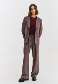 Hnedý károvaný dvojdielny oblek s nohavicami s voľnými nohavicami. Sako má tvarované ramená a výrezové klopy, doplnené vínovým topom.