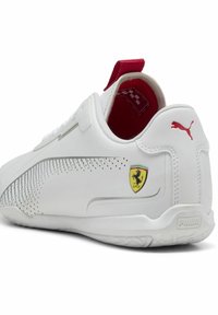 Bijele Puma tenisice s crvenim detaljem na peti, perforiranim dizajnom na vanjskoj strani i istaknutim Ferrari logom.