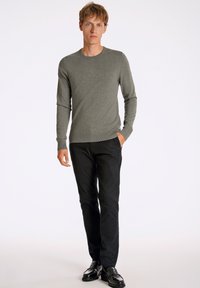 Szary sweter z długim rękawem z prążkowanym okrągłym dekoltem, zestawiony z czarnymi, dopasowanymi spodniami i błyszczącymi czarnymi butami, na tle jednolitego białego tła.