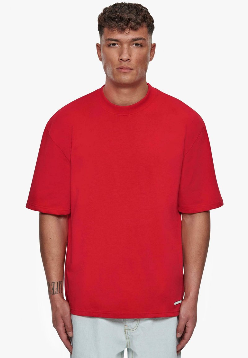 Rotes, übergroßes Baumwoll-T-Shirt mit kurzen Ärmeln und rundem Halsausschnitt. Verfügt über ein Label-Detail nahe dem Saum. Einfarbig, ohne Muster.