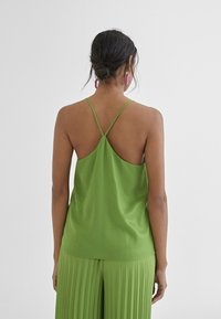 Groene satijnen camisole met dunne straps, met een rugloze ontwerp en een zachte textuur, gecombineerd met een geplooide groene rok.