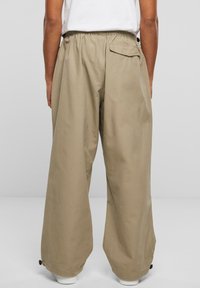 Pantalons larges en tissu beige clair, dotés d'une taille élastique, d'une poche arrière et d'un ourlet ajustable avec des fermetures à toggles.