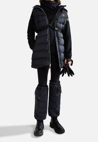 Gilet imbottito nero con cappuccio, chiusura con zip e cinturino regolabile. Abbbinato a gambaletti imbottiti e stivali neri con lacci.