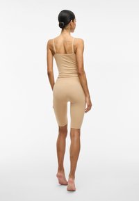 Top sin mangas elástico de color beige claro combinado con pantalones cortos de ciclista a juego, diseño ajustado con tirantes finos, textura suave y corte hasta la rodilla.