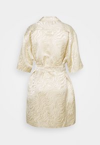 Robe en satin beige avec un motif zébré ondulé, manches courtes, taille ceinturée et poches latérales. Texture lisse et design décontracté.