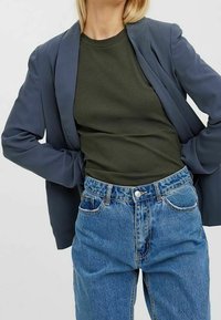 Marinblå blazer över en mörkgrön ribbad topp, tillsammans med högmidjade ljusblå jeans. Funktioner inkluderar en skräddarsydd passform och knappstängning.