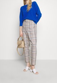 Blå stickad tröja, rutiga beiga och bruna högmidjade byxor, vita öppna klackar och en liten beige handväska.