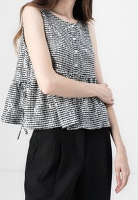 Zwart-wit geruit mouwloos topje met een ronde hals, knoopdetails en een geplooemde zoom, gecombineerd met losse zwarte broek.