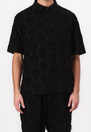 Polo noir à manches courtes en tissu texturé avec un motif discret de logos. Il possède un col classique et une patte de boutonnage à trois boutons.