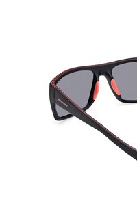 Gafas de sol negras con lentes grises, que presentan un diseño elegante, acentos rojos a lo largo del marco y en las almohadillas de la nariz. Estilo ligero y deportivo.
