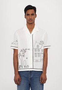 Camisa blanca de manga corta con diseños bordados en negro de casas y naturaleza, con cuello estructurado y cierre de botones. Tejido texturizado.