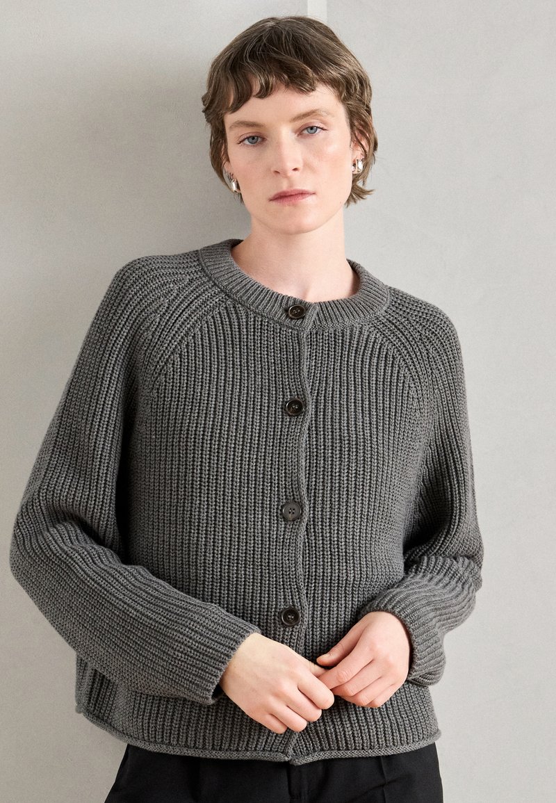 Γκρι πλεχτό cardigan με στρογγυλή λαιμόκοψη, μακριά μανίκια και καφέ κουμπιά. Διαθέτει ραβδωτή υφή και άνετη εφαρμογή.