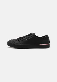 Zapatillas negras con parte superior de sintético suave, puntera redonda, diseño de cordones y un sutil acento a rayas en rojo, blanco y azul en la suela.