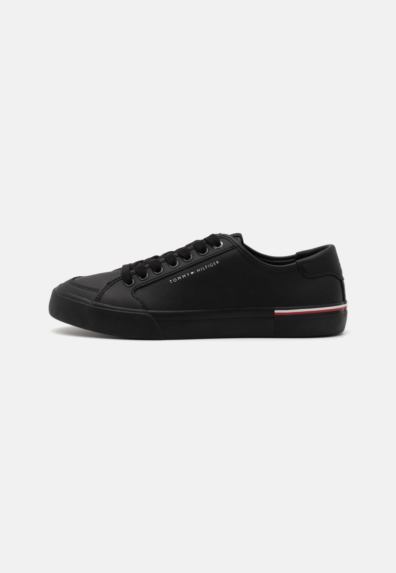 Zapatillas negras con parte superior de sintético suave, puntera redonda, diseño de cordones y un sutil acento a rayas en rojo, blanco y azul en la suela.