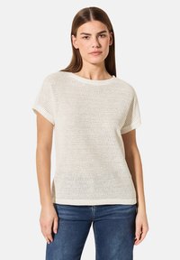 Lätt, krämfärgad stickad t-shirt med korta ärmar, rund halsringning och ett texturerat, öppet vävmönster. Matchas med blå jeans.