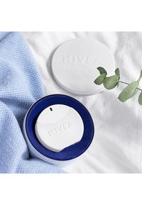 NIVEA Eau de Toilette Spray in weißem Gehäuse in einer runden Box mit blauer Innenauskleidung, neben dem Deckel und einem grünen Eukalyptuszweig auf einem weißen Stoff.