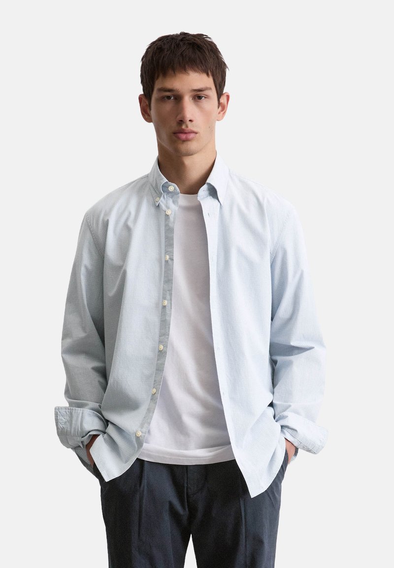 Lichtblauwe overhemd met een subtiele ruitpatroon, open gedragen over een wit T-shirt. Relaxte pasvorm, lange mouwen en zachte stof.
