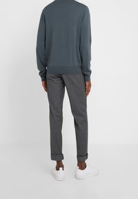 Maglione grigio lavorato a maglia con bordo a coste abbinato a pantaloni grigi a fantasia e sneaker bianche. Cuffia visibile sui pantaloni, texture liscia.