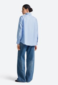 Light blue striped shirt with ruffled collar and long sleeves, paired with wide-leg blue jeans. The fabric appears smooth with a casual fit.