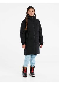 Cappotto imbottito nero con colletto alto, chiusura con zip e tasche laterali. Indossato con jeans blu chiaro e stivali neri con accenti rossi.