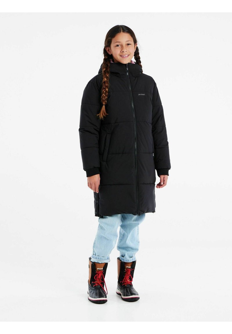 Cappotto imbottito nero con colletto alto, chiusura con zip e tasche laterali. Indossato con jeans blu chiaro e stivali neri con accenti rossi.