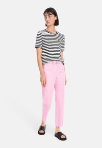 Black and white striped t-shirt with a pineapple emblem, paired with pink tailored pants and black slide sandals.