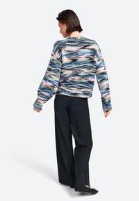 Meerkleurige gebreide trui met golvende patronen in blauw, groen, roze en zwart. Heeft een ronde halslijn en oversized mouwen. Gecombineerd met zwarte broek.