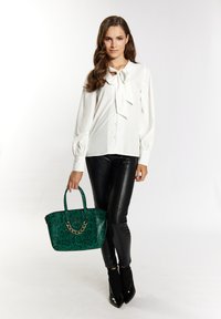 Blusa bianca con dettaglio fiocco, abbinata a pantaloni neri effetto pelle. Tiene una borsa a tracolla verde con motivo serpente e dettagli in catena.