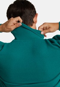 Turkusowy sweter z wysokim kołnierzem, wykonany z gładkiego materiału. Kołnierz jest odchylony, ukazując teksturę prążkowaną oraz detale szycia.