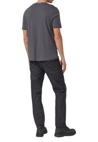 Szara bawełniana koszulka z okrągłym dekoltem, zestawiona z czarnymi dżinsami. Projekt jest prosty, z prostym krojem i bez widocznych logo.