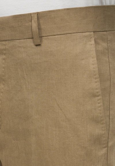Κοντινό πλάνο χακί λινών παντελονιού που δείχνει μέση, θηλιά για ζώνη, μπροστινή τσέπη και υφή υφάσματος.