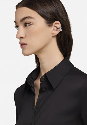 Hõbekõrvarõngas väikese ümmarguse aktsendiga, kantud kõrvadel; modell musta klassikalise kraega särk seljas.