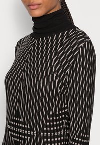 Schwarzer Rollkragenpullover mit geometrischem Muster in Creme und Schwarz, mit gerippter Textur und figurbetonter Silhouette.