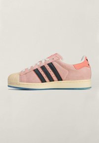 Różowe zamszowe trampki z czarnymi paskami, gumowym noskiem i kremową podeszwą. Posiadają teksturowaną cholewkę oraz białe sznurowadła.