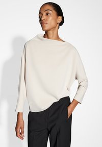 Top cremoso e morbido con scollatura a barca e maniche a tre quarti, abbinato a pantaloni neri sartoriali. Texture liscia e design minimalista.