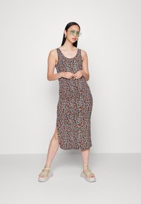 Vestido tanque floral preto com padrões multicoloridos, até ao joelho, com racha lateral. Combinado com sandálias leves e óculos verdes oversized.