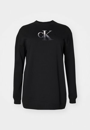 Mustmust mustriba, millel on ümmargune kaelus, pikad varrukad ja hõbedast niidist logo ees. Sile tekstuur, lõdva lõikega.