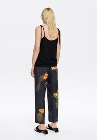Black sleeveless top with thin straps, paired with navy pants featuring an orange floral pattern, and black block-heeled sandals.