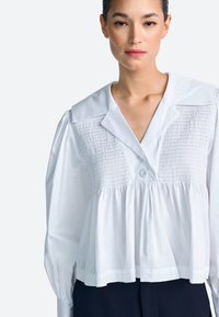 Fehér pamut blúz nagy gallérral, gumírozott testtel és bő ujjakkal. Elöl gombos részlet.