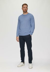 Niebieski sweter o teksturowanym wykończeniu z okrągłym dekoltem, w połączeniu z ciemnoniebieskimi spodniami i białymi trampkami. Prosty design i luźny krój.