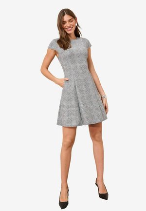 Rochie gri din țesătură tweed cu un corset ajustat, fustă evazată și mâneci tip capac; are buzunare și un finisaj texturat, asortată cu tocuri negre.