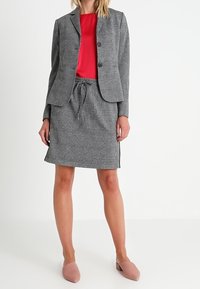 Blazer e gonna grigia a motivi abbinati a una maglietta rossa, con vita regolabile e ballerine rosa solide.