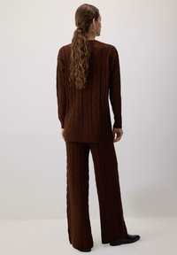 Ruskea kaarrokepaitoja ja siihen sopivat leveälahkeiset housut. Kankaassa on tekstuurimaista kuviointia, ja siinä on ribatut hihansuut ja helmat.