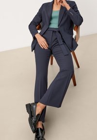 Tmavě modrý oblek s přiléhavým sako a kalhotami s vysokým pasem a širokými nohavicemi. Doplněno mintově zeleným žebrovaným topem a černými lesklými botami.