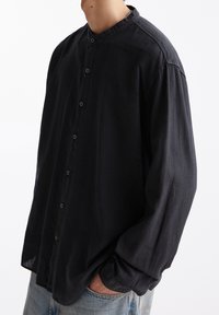 Zwarte, langesleeve knoopshirt met een Chinese kraag, gemaakt van zachte stof, met knoppen aan de voorkant en een relaxte pasvorm.