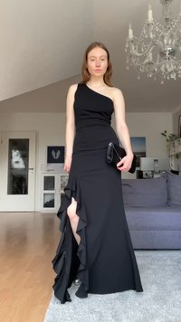 Vestido de evening preto com um ombro, corpete justo e barra com volantes. Apresenta um fenda alta e tecido liso e elástico.