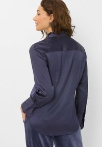 Navyblaue Satinbluse mit glänzender Oberfläche, langen Ärmeln und abgerundetem Saum. Verfügt über ein schlichtes Design mit minimalen Details.