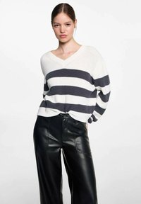 Bílo-námořnický pruhovaný pletený svetr s výstřihem do V, kombinovaný s černými koženými kalhotami s vysokým pasem; volný střih a texturovaná tkanina.