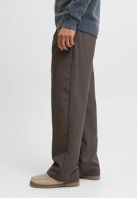 Pantalons marron à jambes larges en tissu lisse, présentant une coupe droite et un ourlet retroussé. Assortis à des chaussures de style mocassins beiges.